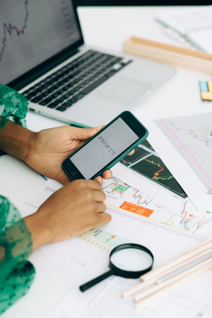 A close-up view of a woman using a smartphone to examine business data shown through charts and graphs.
